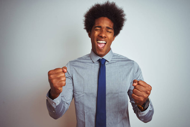 Amerykański człowiek biznesu z Afro włosy noszenia koszuli i krawat na białym tle, bardzo szczęśliwy i podekscytowany robi gest zwycięzcy z ramion podniesione, uśmiechając się i krzyczeć na sukces. Koncepcja obchodów. - Zdjęcie, obraz