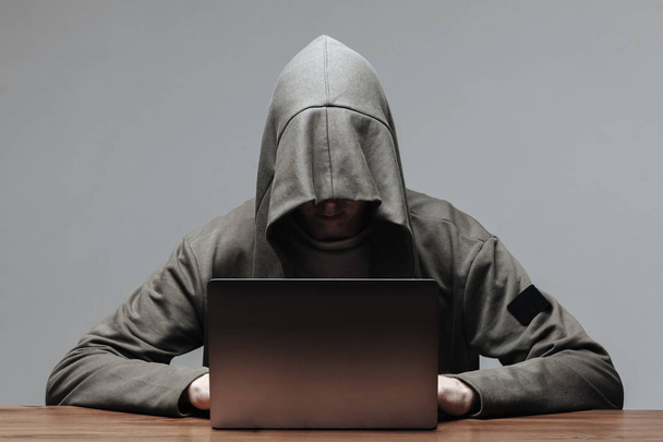 Χάκερ σε μια κουκούλα χωρίς πρόσωπο κάθεται σε ένα φορητό υπολογιστή - Φωτογραφία, εικόνα