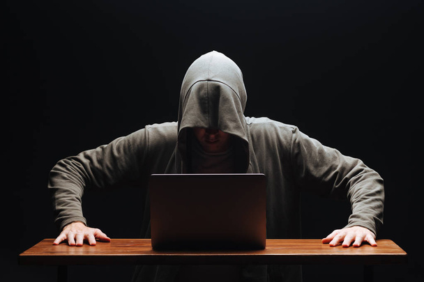 Hacker in a hood with a laptop on a black background - Фото, зображення