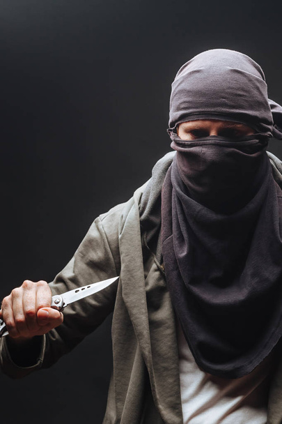  criminoso em uma máscara ameaça com uma faca o fundo escuro
 - Foto, Imagem