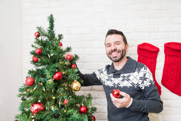 Good looking man adorning Christmas tree with baubles at home - Photo, Image