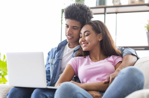 Glimlachend Afrikaans tiener paar ontspannen en kijken naar film op laptop - Foto, afbeelding