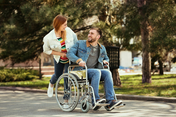 Νέος άνθρωπος σε αναπηρικά αμαξίδια και χαρούμενη γυναίκα στο πάρκο - Φωτογραφία, εικόνα