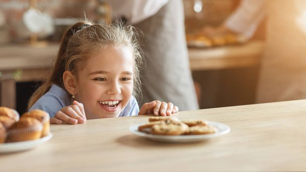 Schattig klein meisje kijkt naar cookies met verlangen - Foto, afbeelding