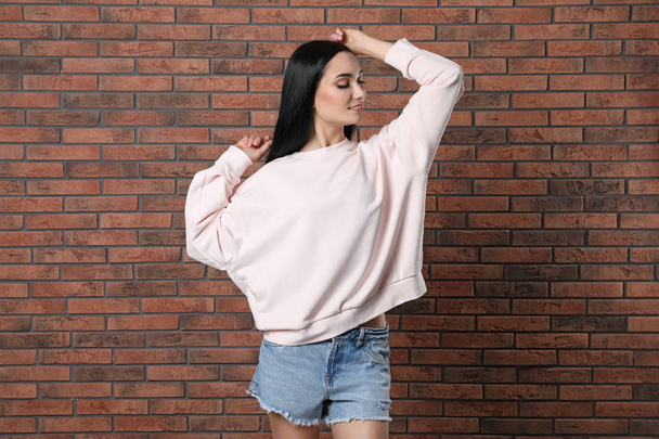 Portrait of young woman in sweater at brick wall. Mock up for design - Foto, Bild