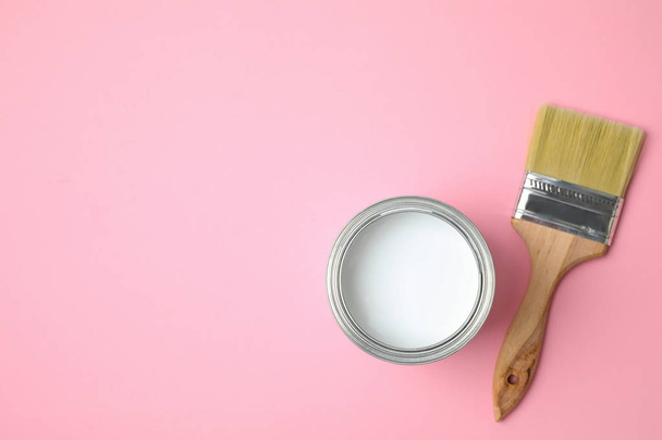 Open can with white paint and brush on pink background, flat lay. Space for text - Фото, зображення