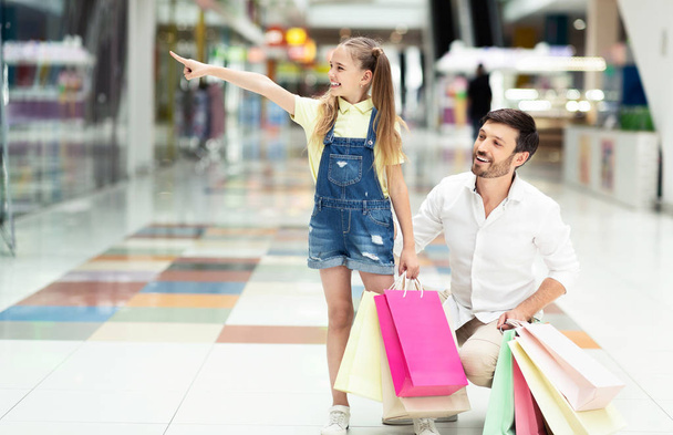 Dziewczyna wskazując na sklep okno chodzenie z father w Mall - Zdjęcie, obraz