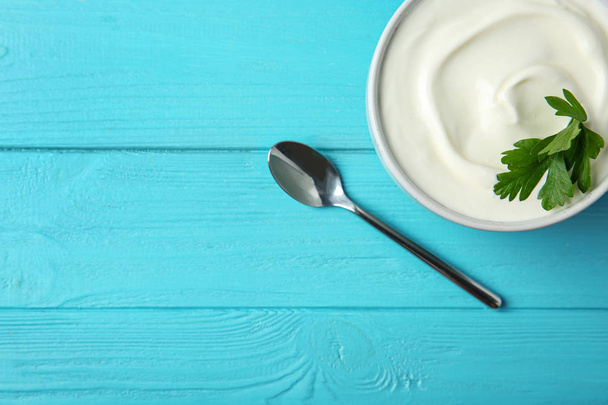 Bowl of fresh sour cream with parsley and spoon on light blue wooden table, flat lay. Space for text - Zdjęcie, obraz
