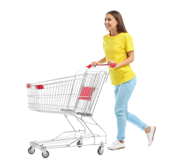 Young woman with empty shopping cart on white background - Fotoğraf, Görsel