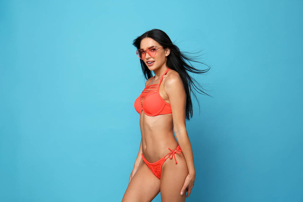 Beautiful young woman in stylish bikini with sunglasses on light blue background - Photo, Image