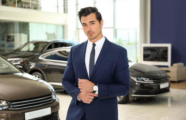 Young salesman near new car in modern dealership - Фото, изображение