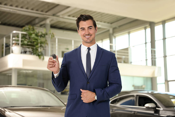 Young salesman with car key in modern dealership - Foto, Imagen
