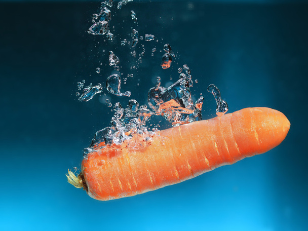 Carrot in the water splash over blue - Фото, изображение