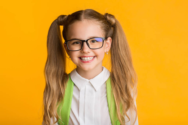 Портрет умной школьницы, улыбающейся в камеру на жёлтом фоне
 - Фото, изображение