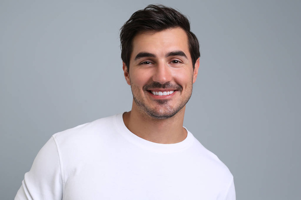 Portrait of handsome young man in white t-shirt on grey background - Foto, Imagem