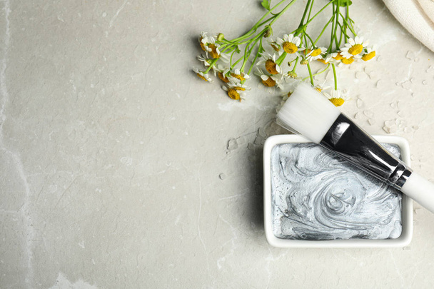 Professional face mask with brush and flowers on light gray marble table, flat lay. Space for text - Photo, Image