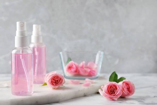 Bottles with rose essential oil and flowers on marble table, space for text - 写真・画像