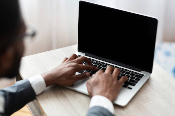Zwarte zakenman typen op laptop met blanco scherm - Foto, afbeelding