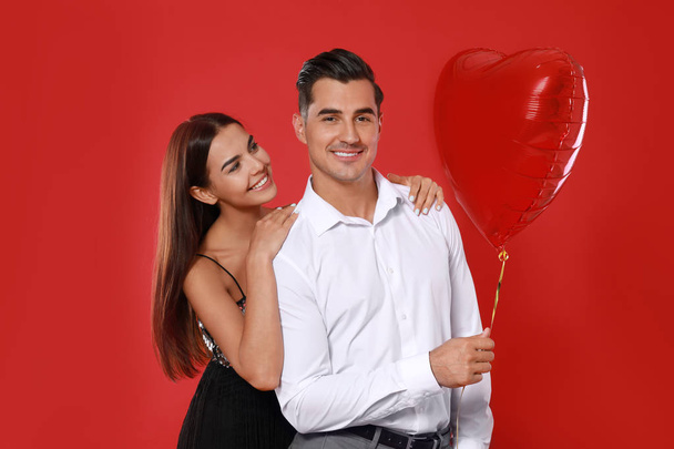 Beautiful couple with heart shaped balloon on red background - Foto, imagen