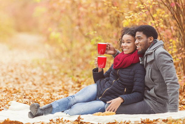 Autumn picnic. Afro couple drinking hot coffee - 写真・画像