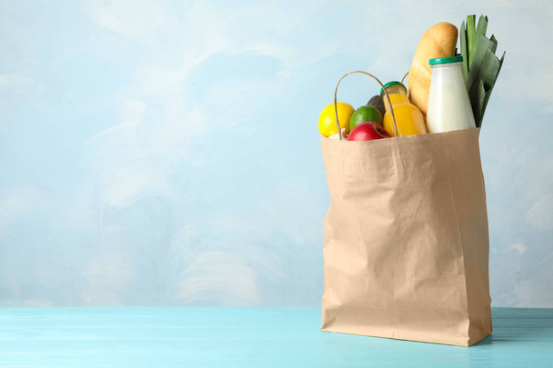 Paper bag with groceries on wooden table against light blue background. Space for text - Foto, imagen