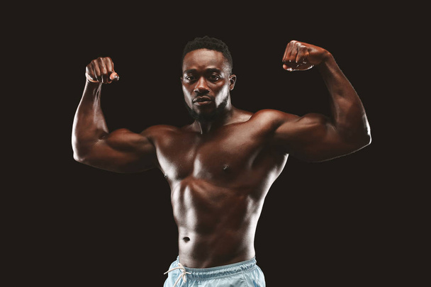 Athletic african guy flexing muscles over black studio background - Foto, immagini