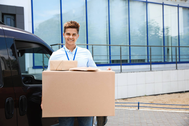 Young courier holding parcels near delivery car outdoors. Space for text - Foto, imagen
