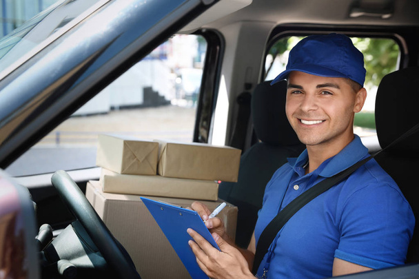 Young courier with parcels and clipboard in delivery car - Foto, Imagen