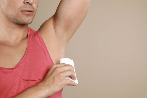 Young man applying deodorant to armpit on beige background, closeup. Space for text - Фото, изображение