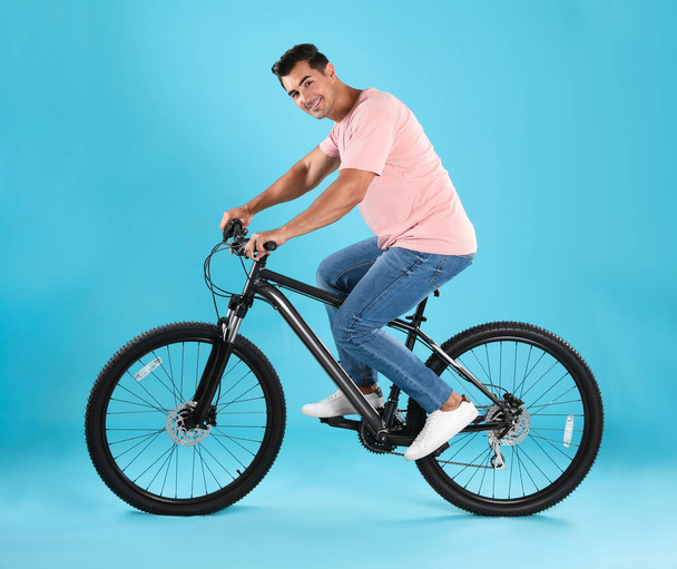 Handsome young man with modern bicycle on light blue background - Φωτογραφία, εικόνα