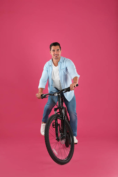 Handsome young man with modern bicycle on pink background - Photo, image