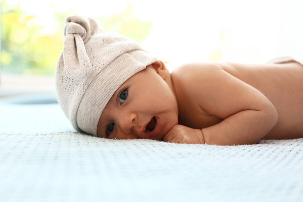 Cute little baby in hat lying on light blue plaid indoors - 写真・画像