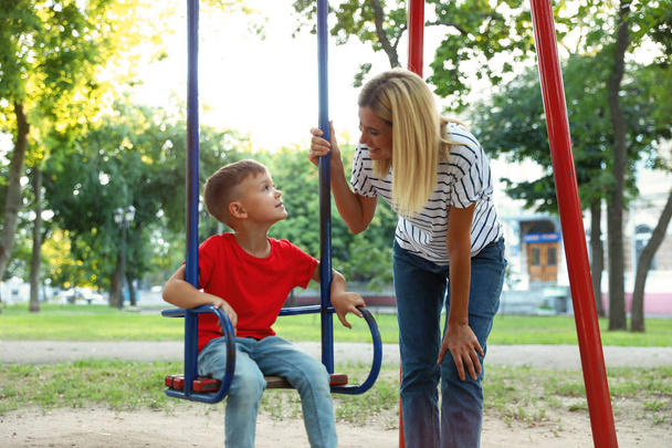 Nanny and cute little boy on swing in park - Фото, зображення