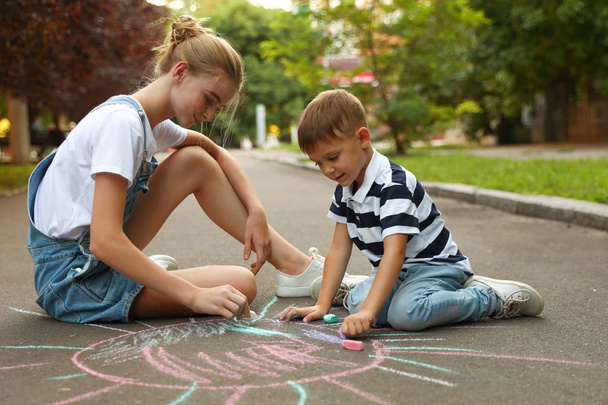 Teen nanny and cute little boy drawing sun with chalks on asphalt - Photo, Image