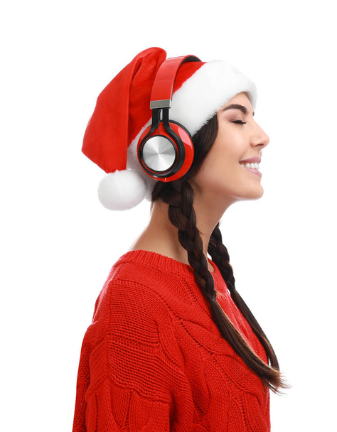 Young woman in Santa hat listening to Christmas music on white background - 写真・画像