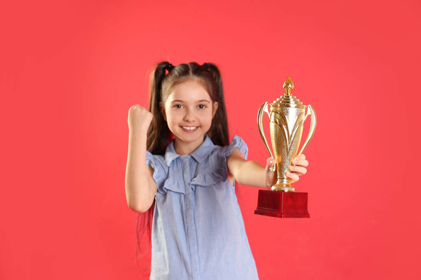 Happy girl with golden winning cup on red background - Φωτογραφία, εικόνα