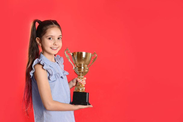 Happy girl with golden winning cup on red background. Space for text - Фото, изображение