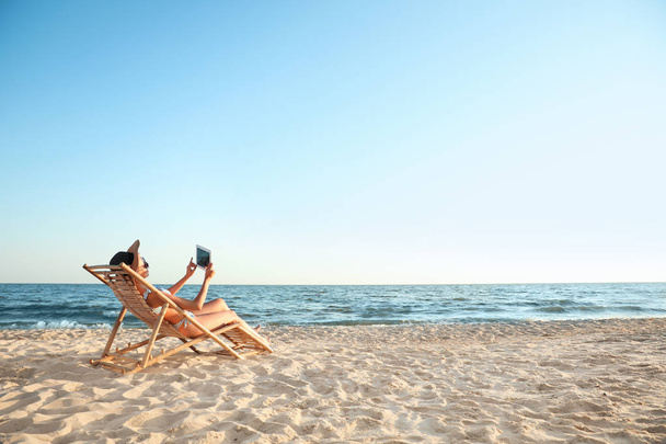 Young woman with tablet relaxing in deck chair on beach - Photo, image