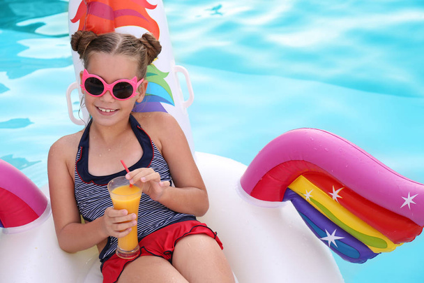 Happy girl with drink on inflatable unicorn in swimming pool - Фото, зображення