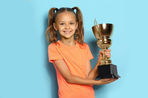 Happy girl with golden winning cup on blue background - Photo, Image