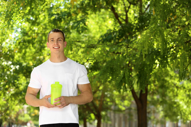 Athletic young man with protein shake at green park - Fotoğraf, Görsel