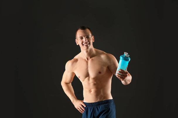 Athletic young man with protein shake on black background - Фото, изображение