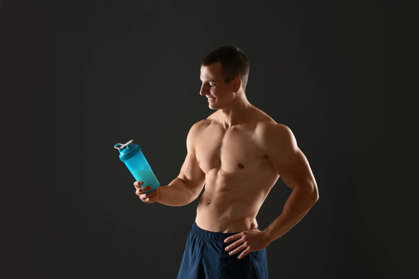Athletic young man with protein shake on black background - Φωτογραφία, εικόνα