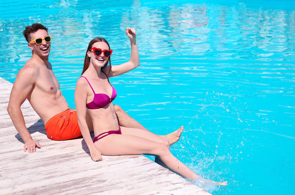 Happy young couple sitting near swimming pool - Photo, Image