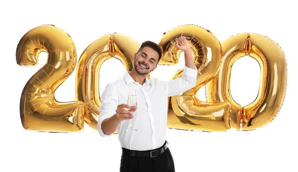Happy young man with glass of champagne near golden 2020 balloons on white background. New Year celebration - Foto, Imagen