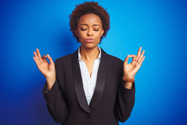 afroamericano business executive donna su sfondo blu isolato rilassarsi e sorridere con gli occhi chiusi facendo gesto di meditazione con le dita. Concetto yoga
. - Foto, immagini
