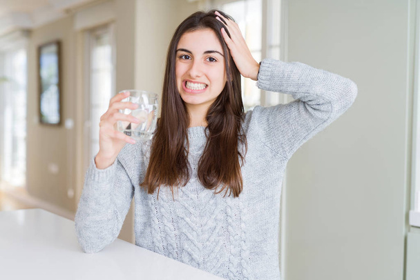 Beautiful young woman drinking a fresh glass of water stressed with hand on head, shocked with shame and surprise face, angry and frustrated. Fear and upset for mistake. - Foto, afbeelding