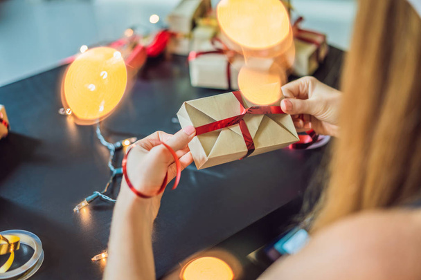 Young woman is packing presents. Present wrapped in craft paper with a red and gold ribbon for christmas, birthday, mothers day or valentine - Zdjęcie, obraz