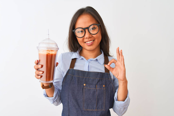 Čínská žena nosí brýle zástěra pití smoothie přes izolované bílé pozadí dělá v pořádku znamení s prsty, vynikající symbol - Fotografie, Obrázek