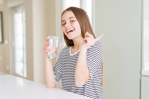 Belle jeune fille enfant boire un verre d'eau fraîche très heureux pointant avec la main et le doigt sur le côté
 - Photo, image